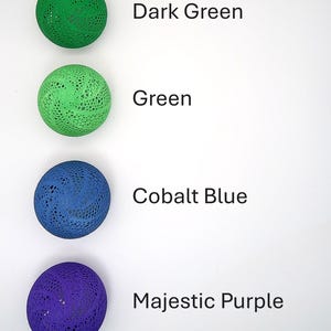 May include: Four decorative balls in different colors: dark green, green, cobalt blue, and majestic purple. Each ball has a lacy pattern.