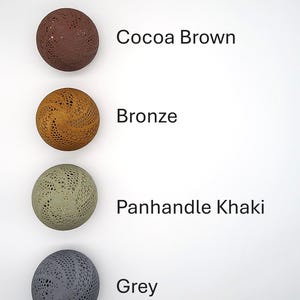 May include: Four round, decorative balls with a lacy pattern. The balls are in the colors cocoa brown, bronze, panhandle khaki, and grey.