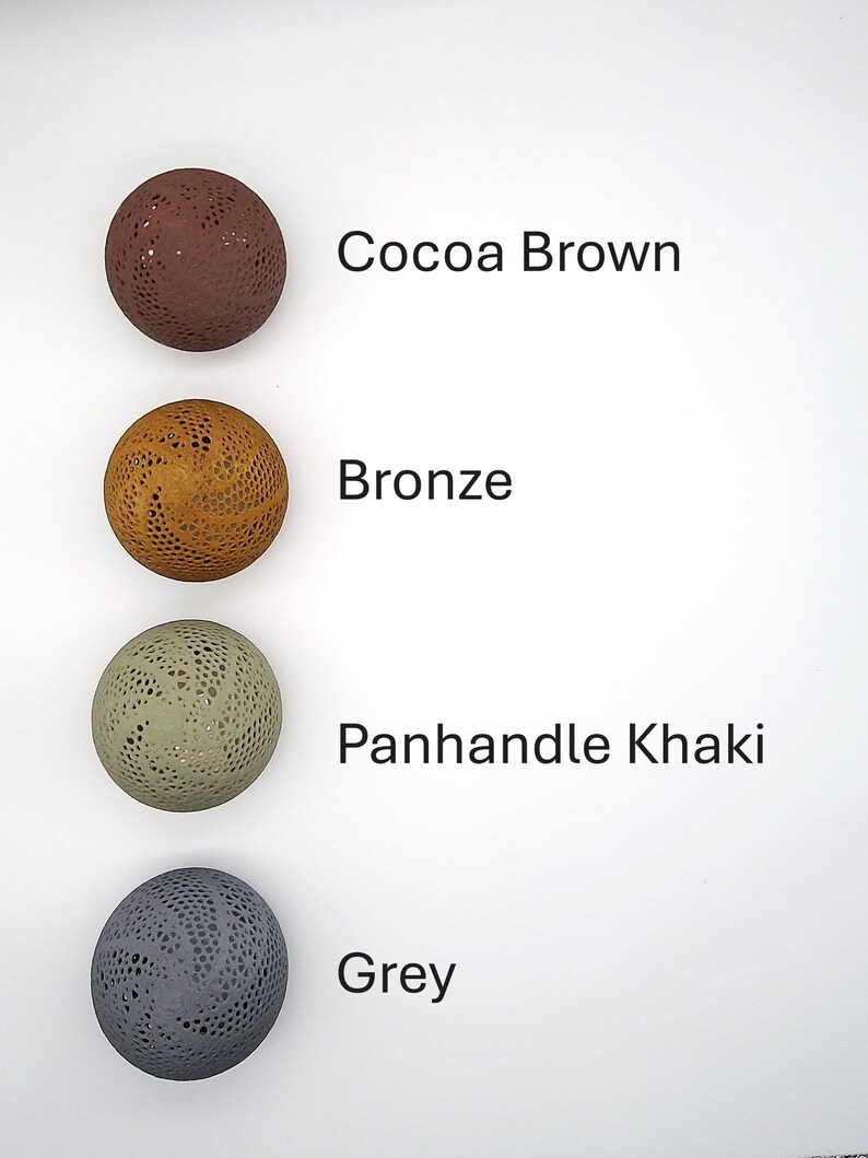 May include: Four round, decorative balls with a lacy pattern. The balls are in the colors cocoa brown, bronze, panhandle khaki, and grey.