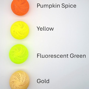 May include: Four decorative balls with a lacy pattern in different colors: pumpkin spice, yellow, fluorescent green, and gold.