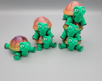 Puede incluir: Una pila de cinco figuras de tortugas verdes y marrones. Las tortugas están apiladas una encima de la otra, con la tortuga más grande en la parte inferior y la más pequeña en la parte superior. Las tortugas tienen ojos grandes y una expresión amigable.