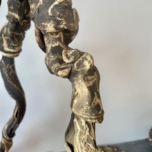 May include: Close-up of a handcrafted, abstract sculpture with a unique, organic form. The sculpture features a dark brown and cream-colored marbled pattern, with a textured surface. The piece has a natural, earthy aesthetic.