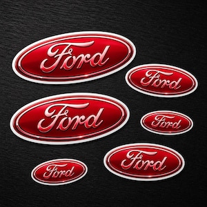 Puede incluir: Colección de emblemas ovalados Ford rojos con efecto cromado y bordes blancos. La escritura Ford es en cursiva. Los emblemas varían en tamaño y están dispuestos sobre una superficie oscura y texturizada.