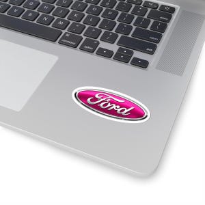 May include: A pink oval sticker with the word "Ford" in silver script. The sticker has a silver border and is placed on a silver laptop.