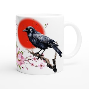 Peut inclure: Une tasse en céramique blanche avec un corbeau noir perché sur une branche avec des fleurs roses. Le corbeau est tourné vers la gauche et l'arrière-plan est un cercle rouge.