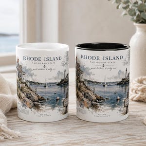 Può includere: Due tazze in ceramica con un design costiero. Le tazze presentano il testo "Rhode Island The Ocean State" e un'illustrazione di un porto con barche a vela, un faro e una cittadina costiera. Una tazza ha l'interno nero.