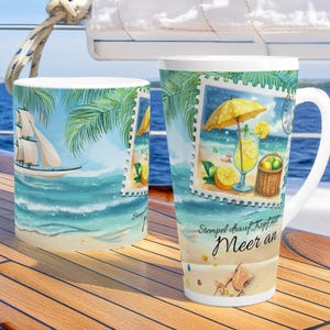 Könnte beinhalten: Zwei weiße Keramikbecher mit Strandmotiven. Ein Becher zeigt ein Segelboot, Palmen und Wellen. Der andere hat eine Strandszene mit Cocktail, Zitronen und Sonnenschirm. Die Becher stehen auf einer Holzoberfläche.