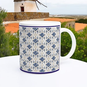 Può includere: Tazza in ceramica bianca con un motivo floreale blu e bianco. La tazza ha un manico bianco e un bordo blu. La tazza è su una superficie bianca, con fogliame verde e un edificio sullo sfondo.