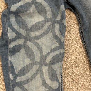 May include: Blue denim jeans with a white bleach design of overlapping circles and squares.