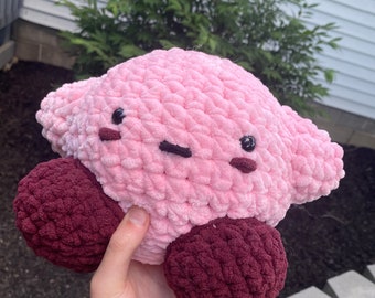 May include: A pink and maroon crocheted plush toy shaped like a star with a cute cartoon face.