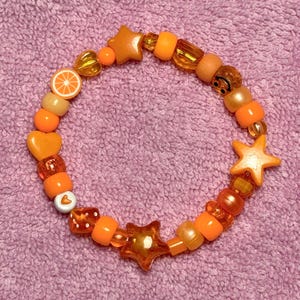 May include: Orange, yellow, and white beaded bracelet with star, heart, and smiley face charms.