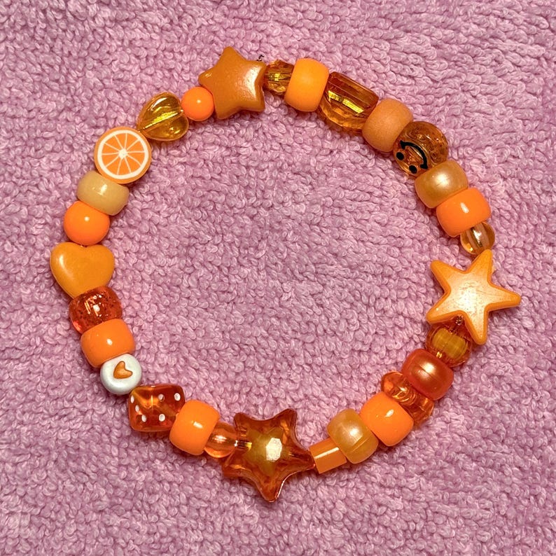 May include: Orange, yellow, and white beaded bracelet with star, heart, and smiley face charms.