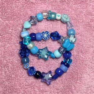 May include: A blue and white beaded bracelet with star, flower, and butterfly charms. The bracelet is made with a variety of different sized beads.