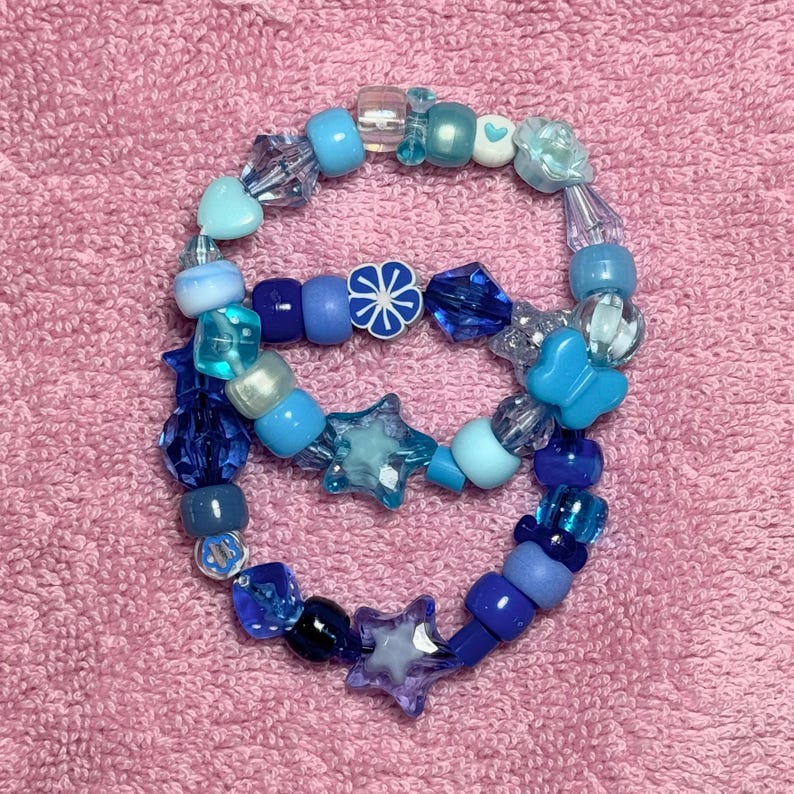 May include: A blue and white beaded bracelet with star, flower, and butterfly charms. The bracelet is made with a variety of different sized beads.