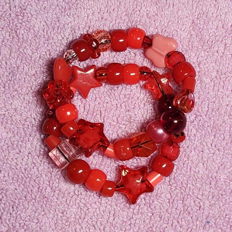 May include: Red and pink beaded bracelet with star and heart charms. The bracelet is made with various sizes and shapes of beads.