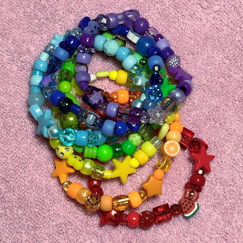 May include: A set of colorful beaded bracelets with rainbow colors, star, fruit, and smiley face charms.