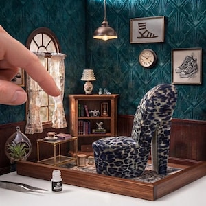 May include: A miniature room diorama featuring a leopard print high-heel shoe chair, a wooden bookshelf with books and a camera, a small side table with a teacup, a hanging pendant light, and two framed wall art pieces depicting footwear.