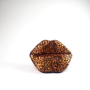 May include: A decorative, plush lip-shaped object with a leopard print pattern. The lips are brown and tan with dark brown spots. The object is on a white background.