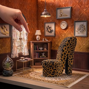 Peut inclure: Une scène de pièce miniature comprenant une chaise en forme de talon haut à motif léopard, une bibliothèque en bois avec des livres et un sablier, une petite table d'appoint en verre avec une tasse, une suspension et des cadres illustrant des chaussures.
