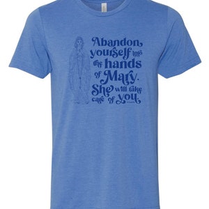 Pu&ograve; includere: T-shirt blu chiaro con un'illustrazione religiosa e il testo: "Abandon yourself into the hands of Mary. She will take care of you."