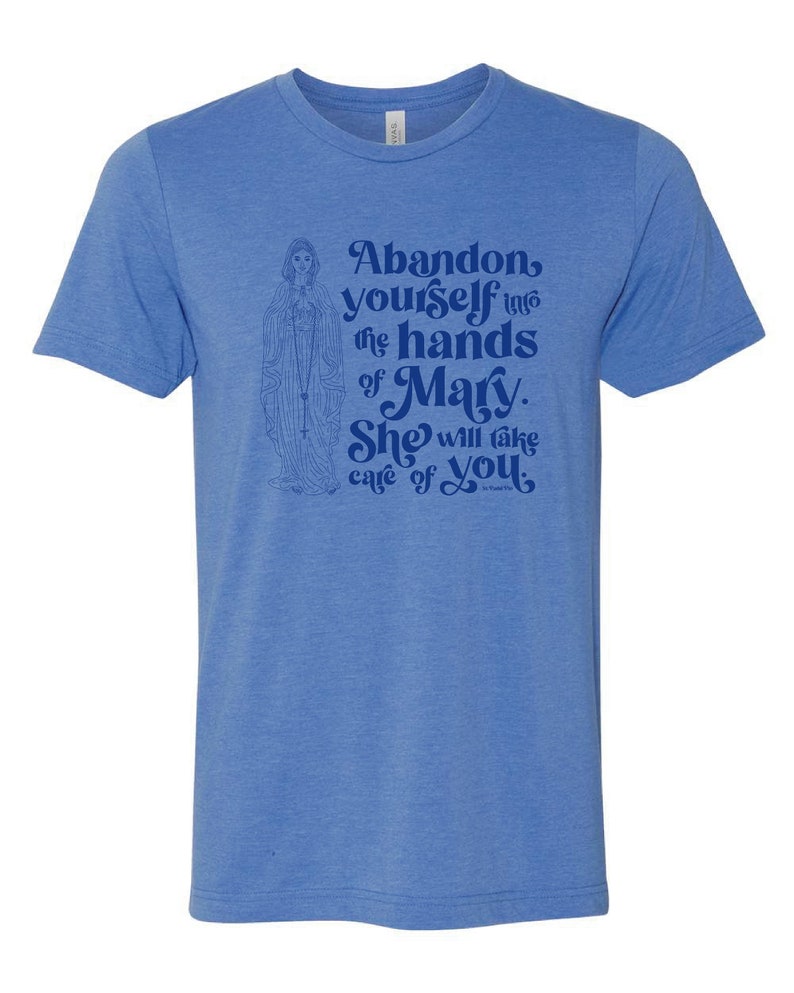 Pu&ograve; includere: T-shirt blu chiaro con un'illustrazione religiosa e il testo: "Abandon yourself into the hands of Mary. She will take care of you."