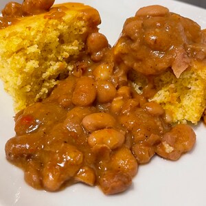 May include: A white plate with two pieces of cornbread and a brown gravy with white beans.