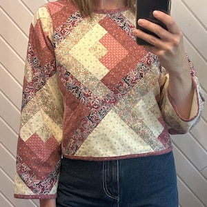 Peut inclure: Haut matelassé avec un motif patchwork dans les tons de rose, crème et gris. Le haut à manches longues présente une encolure ronde et est associé à un jean en denim bleu. Le tissu a un motif floral.