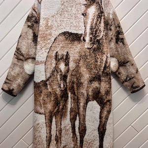 Peut inclure: Un manteau à manches longues arrivant au genou, fabriqué dans une matière texturée semblable à de la polaire dans des tons crème, beige et brun foncé. Le vêtement présente un grand imprimé détaillé d'un cheval et d'un poulain.
