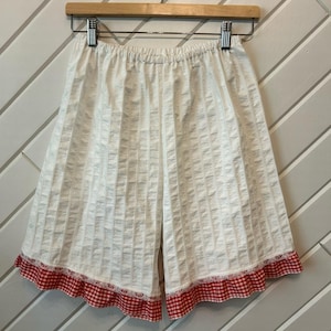 Peut inclure: Short en coton blanc avec une bordure en vichy rouge et blanc. Le short a une taille élastiquée et une coupe ample.