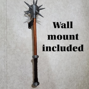 May include: A gray spiked mace with a wooden handle and a black grip, mounted on a wall. The text "Wall mount included" is displayed in black letters.