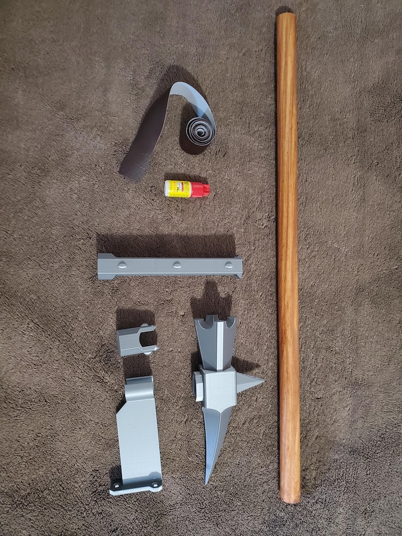 May include: An assortment of craft supplies and components, including a wooden dowel, gray metal pieces, sandpaper, and a small tube of glue. The items are arranged on a brown surface, suggesting a DIY project or craft kit.