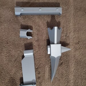 May include: A collection of gray 3D-printed parts, including a long rectangular piece with rounded screw heads, a small U-shaped piece, a flat piece with a right-angle bend, and a complex, pointed tool.