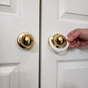 May include: Two white door knobs with gold accents. One knob has a white ring around it.
