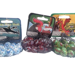 May include: Three bags of marbles with different packaging. One bag has blue and white marbles, another has red and white marbles, and the third has green and red marbles. The packaging features a shark, a rooster, and a dragon. Each bag contains 24 marbles and a shooter marble.