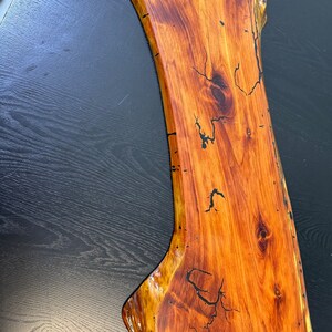 May include: A large, natural wood serving board with a live edge and a dark brown epoxy fill. The board has a natural, rustic look and is perfect for serving cheese, charcuterie, or other appetizers.