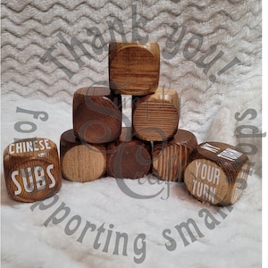May include: A set of eight wooden dice with various phrases printed on them, including "Chinese Subs", "My Turn", and "Your Turn". The dice are stacked in a pyramid shape on a white fuzzy surface.