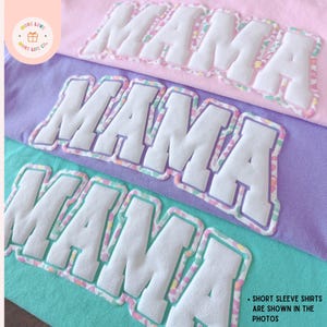 K&ouml;nnte beinhalten: Nahaufnahme von drei kurz&auml;rmeligen Shirts in Pastellfarben: Rosa, Lila und T&uuml;rkis. Jedes Shirt zeigt das Wort "MAMA" in gro&szlig;en, wei&szlig;en, gepolsterten Buchstaben mit einem farbenfrohen Rand. Der Text "SHORT SLEEVE SHIRTS ARE SHOWN IN THE PHOTOS" ist ebenfalls sichtbar.