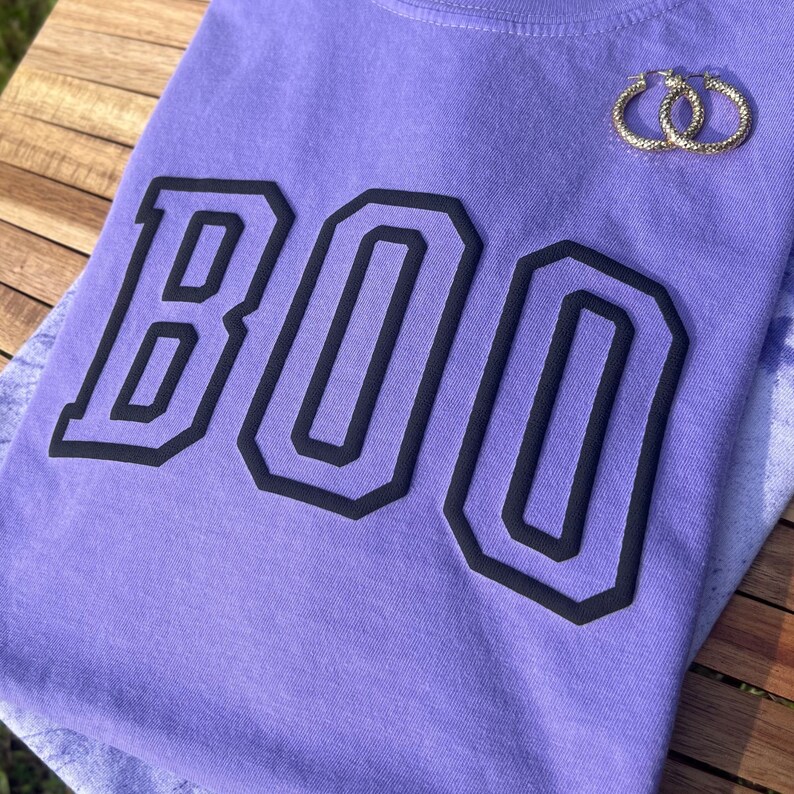 May include: Purple t-shirt with the word "BOO" in black outlined letters.