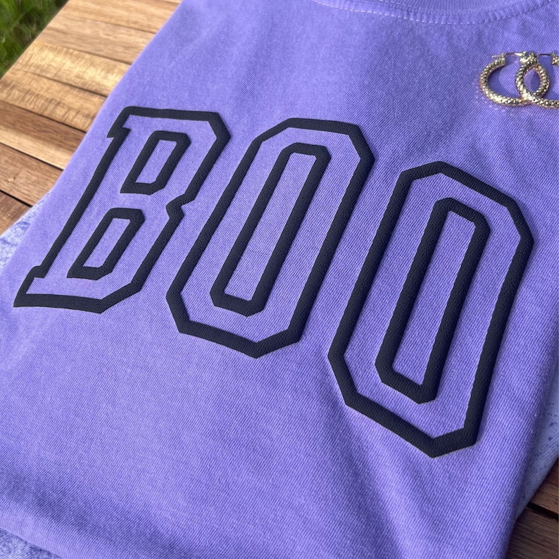 May include: Purple t-shirt with the word "BOO" printed in black outlined letters.