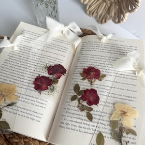 May include: A close-up of an open book with dried flowers pressed between the pages. The book is open to a page with text about a restaurant and a river. The flowers are red, white, and yellow.
