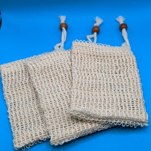 May include: Three white mesh bags with wooden toggles. The bags are stacked on top of each other and are made of a fine, woven material.