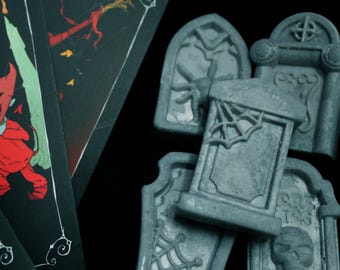 May include: A selection of grey miniature tombstones featuring spiderwebs and a skull, next to dark playing cards with red and green illustrations. The items are set against a black backdrop, creating a spooky Halloween theme.