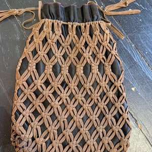 May include: A brown leather drawstring bag with a black lining and a woven pattern. The bag has two long brown leather ties.