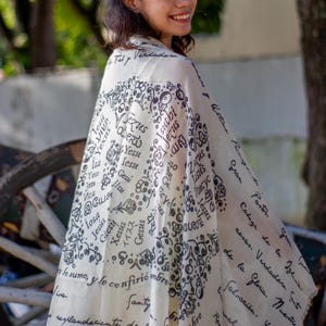May include: A white scarf with black lettering and floral designs. The lettering includes the word "Jesus" in multiple languages. The scarf has a handwritten inscription that reads "a lo sumo, y le confirio" and "resplandeciente de santy".