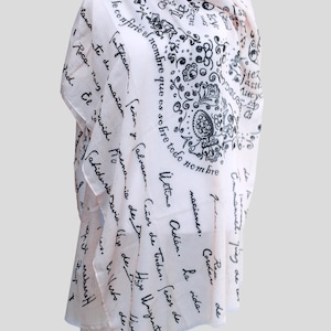 May include: A white scarf with black text and a floral design. The text includes the words "Último Adán", "La vida", "Cantificar", "Señor", "Salvador", "Señor de todas", "Señor de", "lana", "te de", "mañan", "Elavid", "Mena", "Roca", "Raig", "2d", "or", "de Da", "Hiso Uniginite", "de Ho", "Cabiduria Savia lisp de Do", "Hiso del", "Nias", "Ellerto de", "reberet", "T".