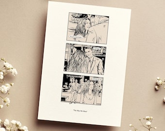 May include: A black and white comic strip print featuring three panels with a couple. The print is on a cream-colored card, with the title "The Way We Were" at the bottom. Delicate white flowers are arranged around the card.