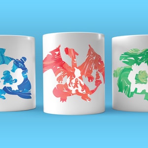 May include: Three white ceramic mugs with colorful abstract designs of popular Pokemon characters. The mugs are arranged in a row from left to right, with the blue mug on the left, the red mug in the middle, and the green mug on the right.