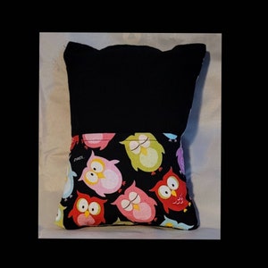 May include: Black pillow with a black fabric front and a back made of black fabric with a colorful owl print. The owls are pink, red, green, and blue with black eyes.