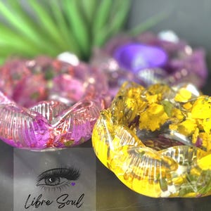 May include: Three resin lotus-shaped bowls. One is filled with pink flowers, another with yellow flowers, and the third with a purple object. The bowls are on a dark surface. The text "Libre Soul" is at the bottom.