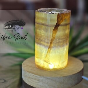 May include: A yellow and brown calcite crystal lamp on a wooden base. The lamp is lit and emits a warm glow.
